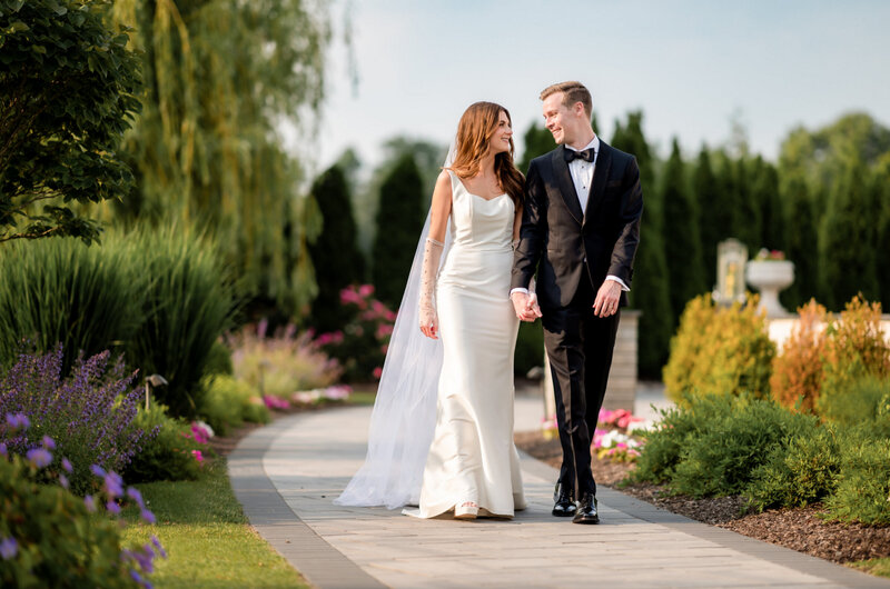 Bride and groom, holding hands walking down a path in the gardens of the mansion on Main Street in Voorhees, New Jersey