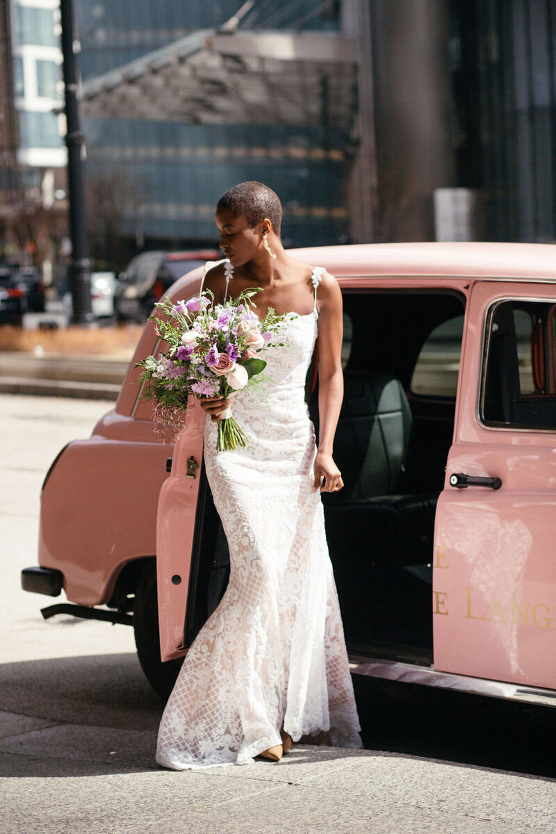 bride steps out of a pink vintage car holding a pink bouquet of flowers