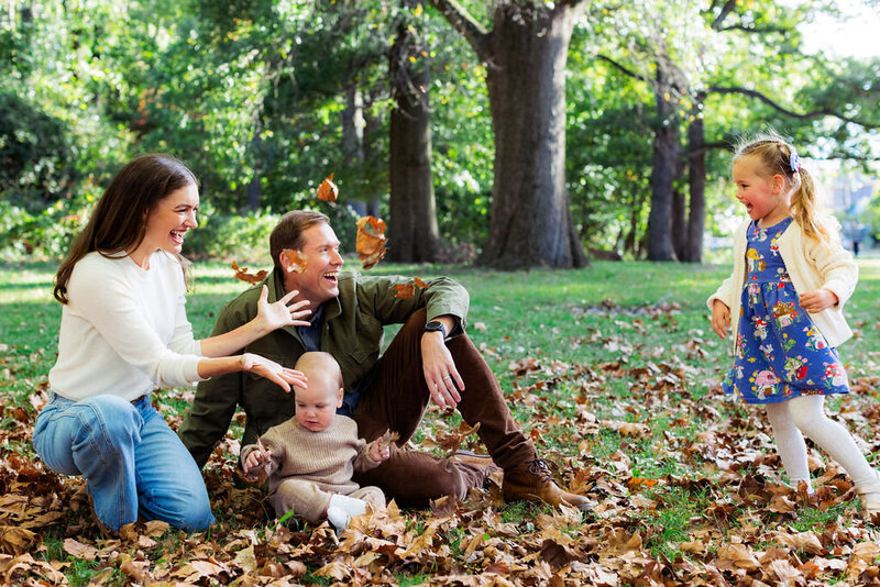 A family plays in the fall leaves together at a park