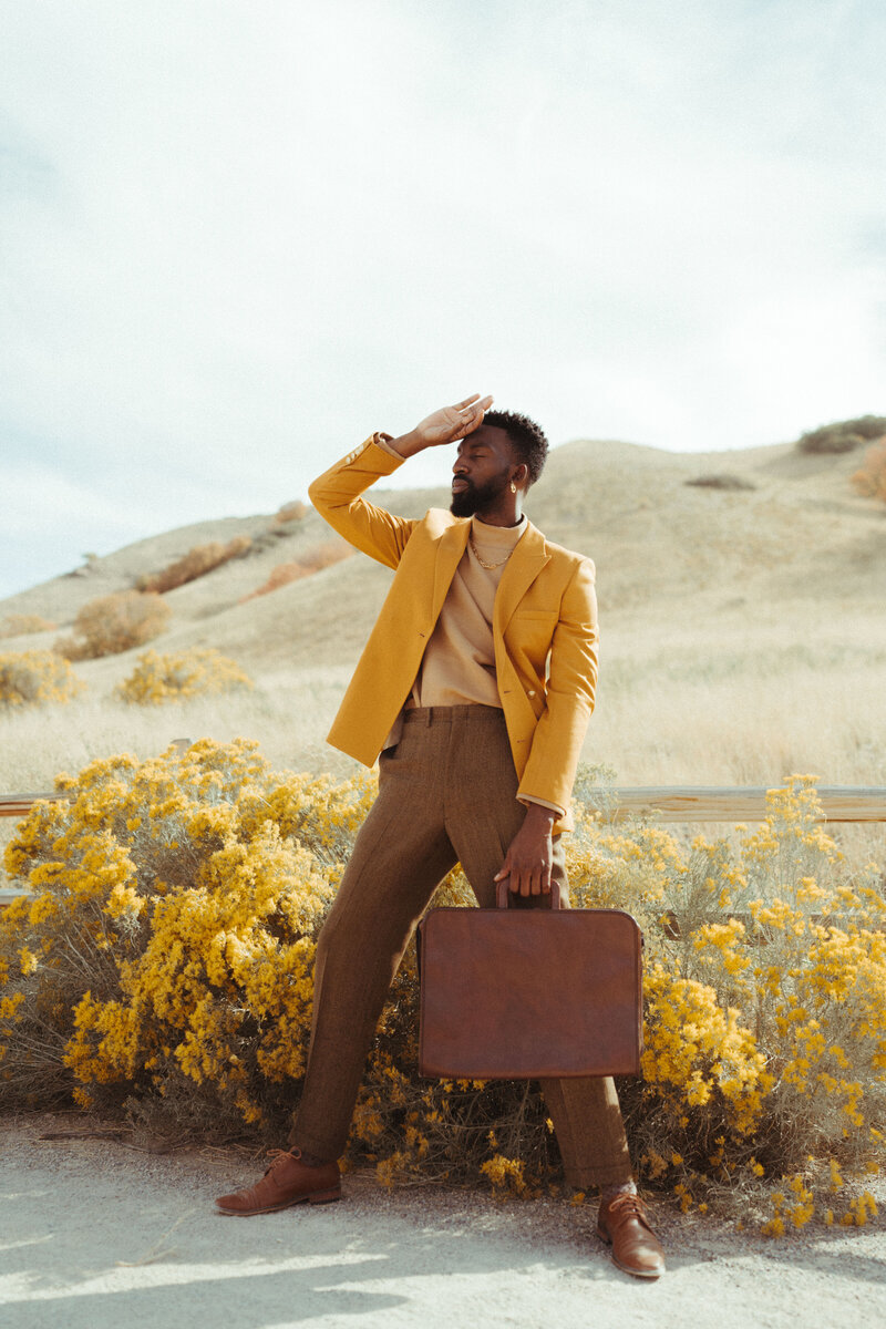 man holding a suitcase in a field with yellow flowers