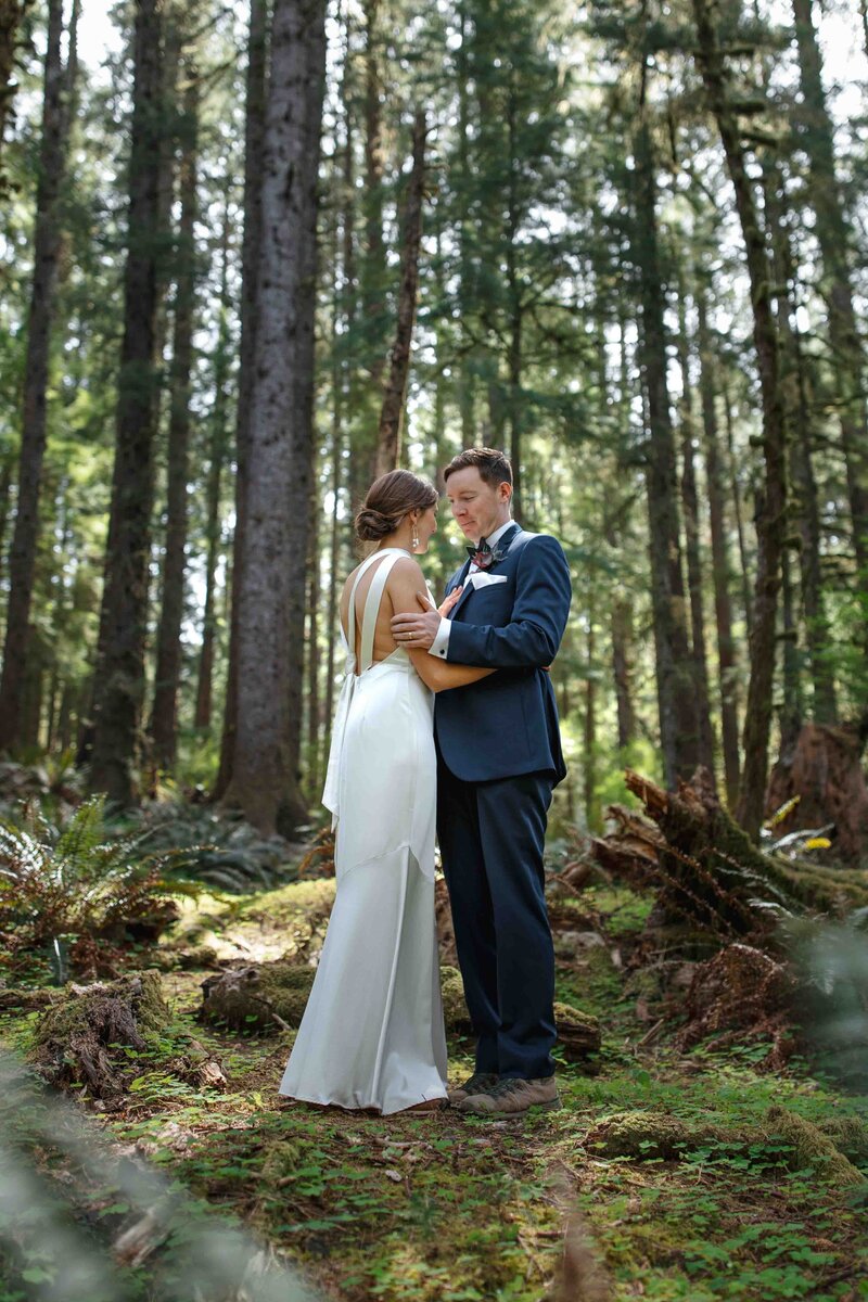 A bride and groom hiking through Ecola State Park during their elopement. They are surrounded by ferns, moss and Doug Fir trees.