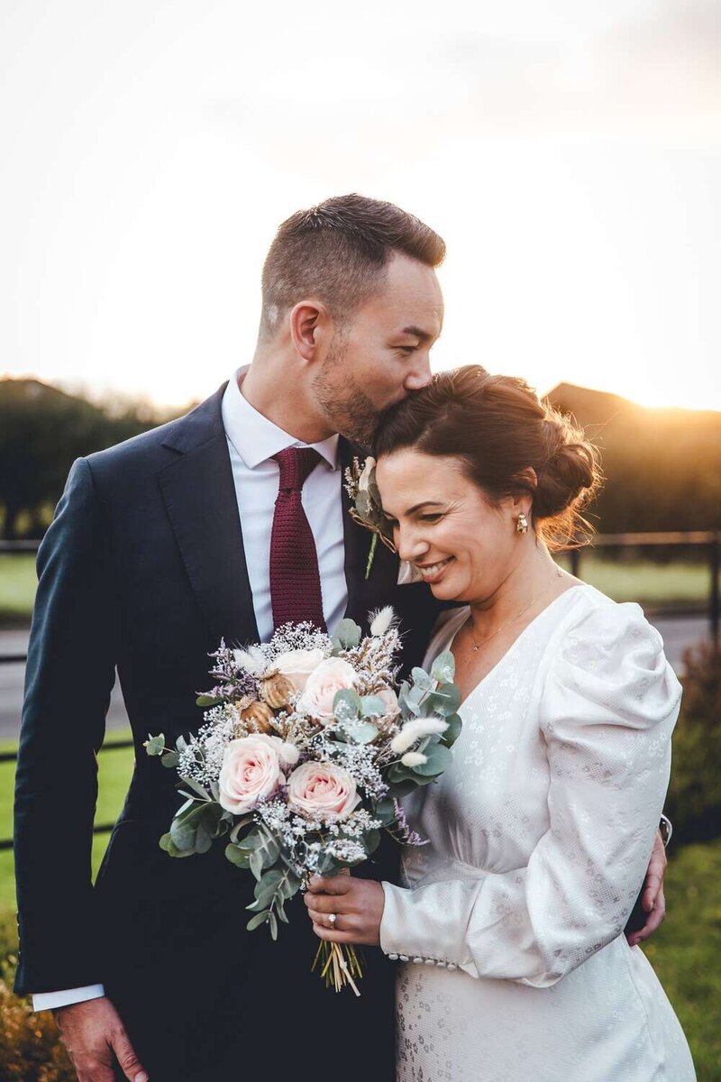 Groom kisses bride on top of her head lovingly