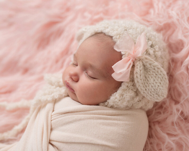 Newborn photo of sleeping baby in bonnet with bow