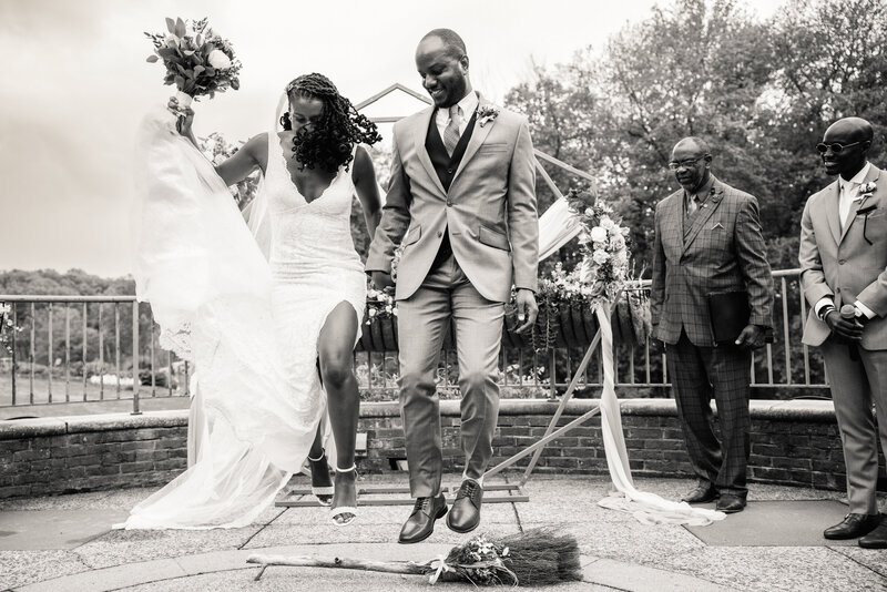 Two newlyweds jump over a broom during their ceremony