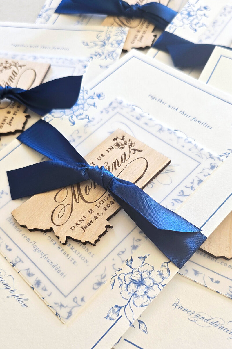 Montana-themed wedding invitation suite with blue floral details, Montana wood magnet, and navy ribbon, designed by stationery artist Seventh and Anderson