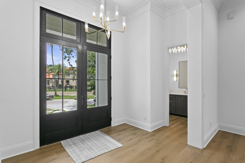 Foyer of bright luxury home picturing dark front doors with large window panes.