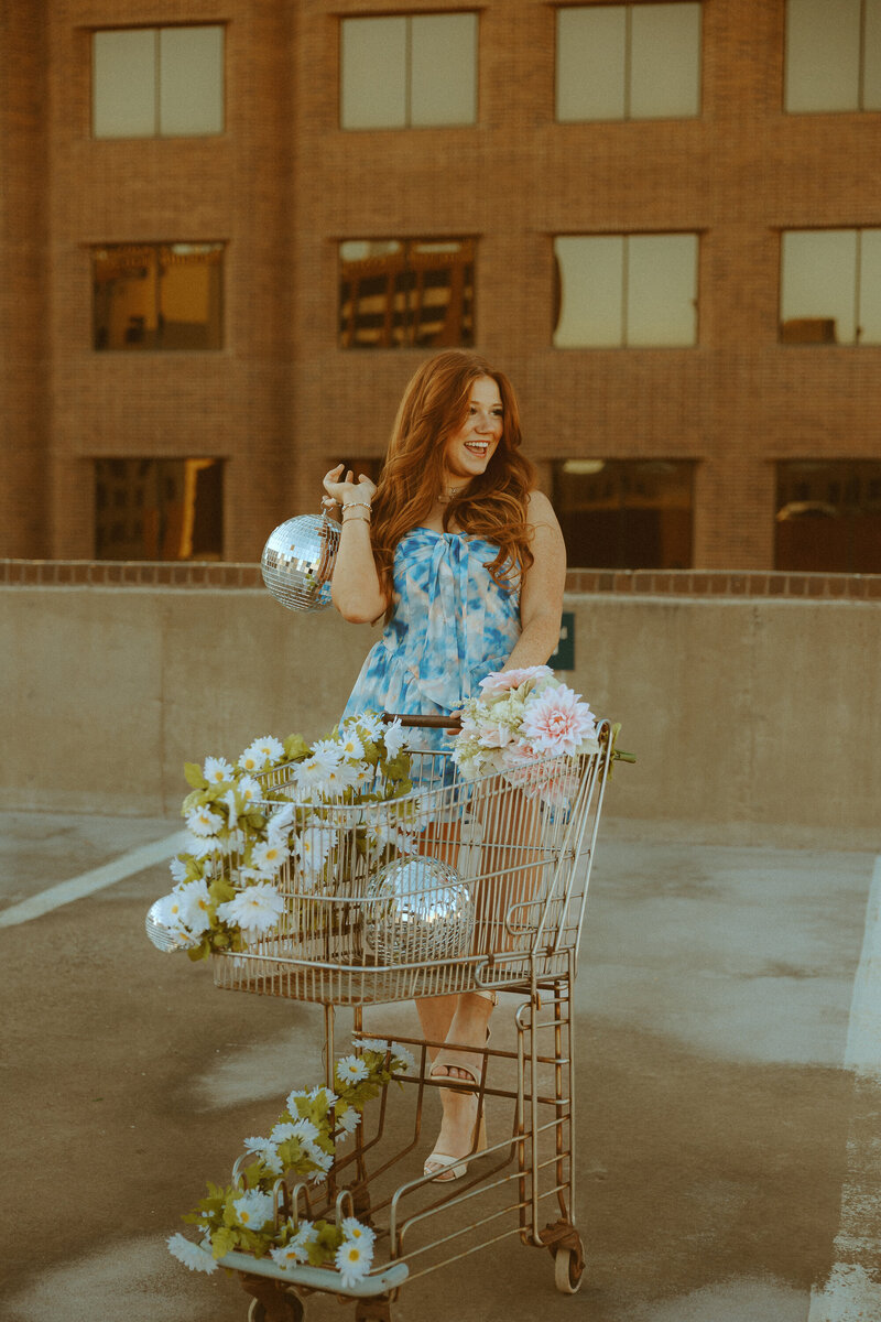 Golden portrait styled shoot with disco balls, florals, and a shopping cart on a rooftop garage in downtown Abilene, TX