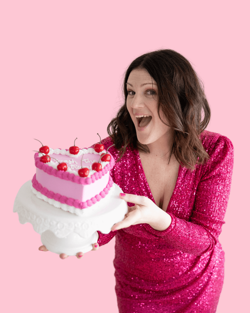 Emily in a pink dress holds a heart-decorated cake, reflecting her vibrant personality as a web designer.