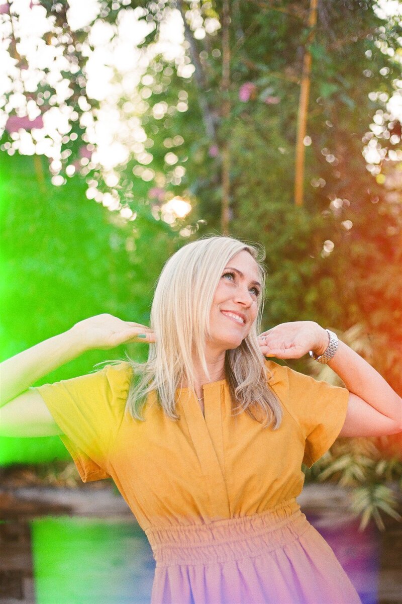 A fun and vibrant woman makes a silly pose while wearing a yellow dress