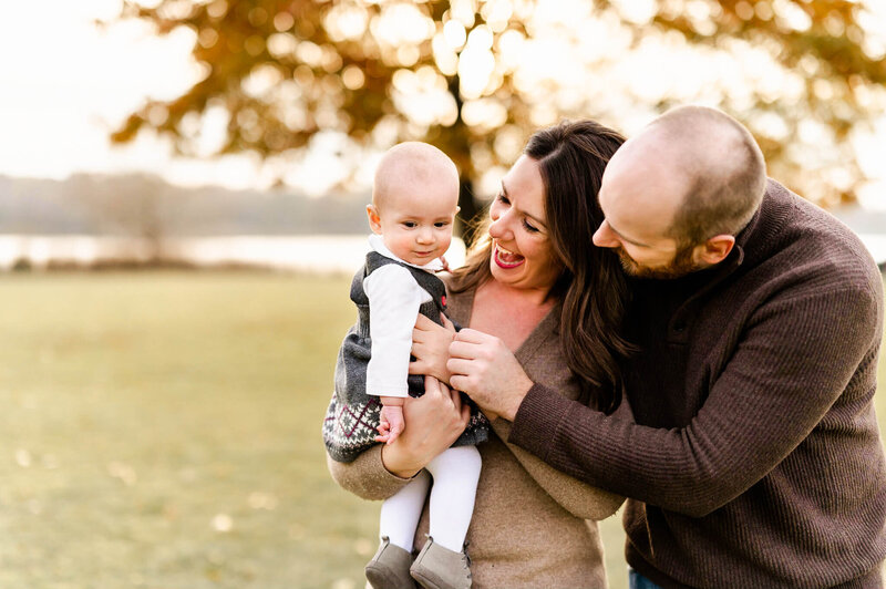 Dad and mom playfully engaging baby as they walk through Busse Woods during a family session near Chicago.