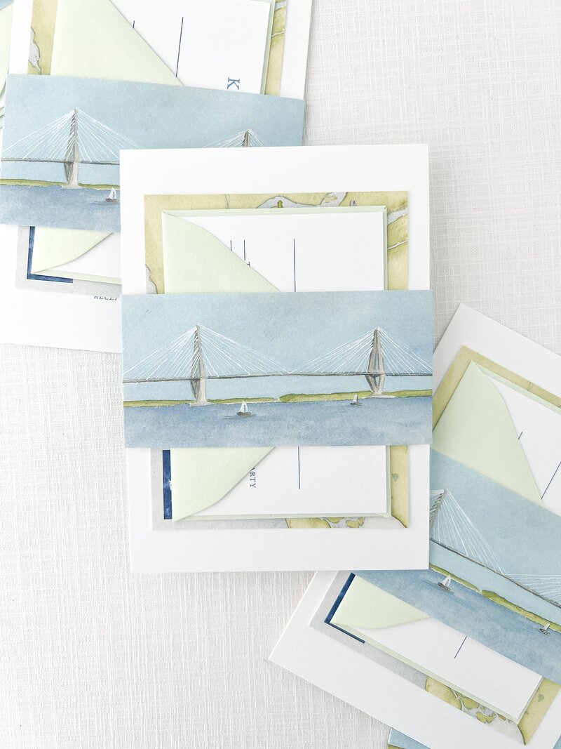 a painting of sailboats printed on the belly band that is wrapped around a wedding invitation suite