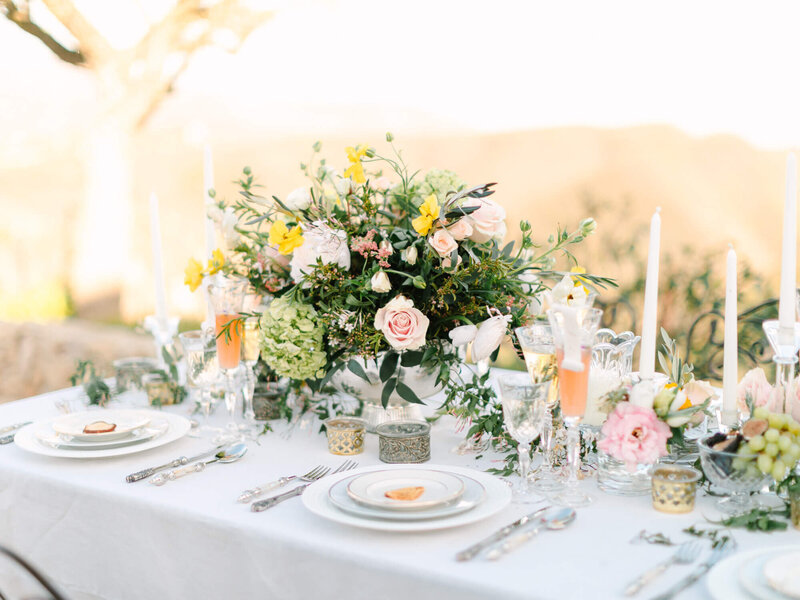 Elegant outdoor table setting with a lush floral centerpiece of pink and yellow blooms. 