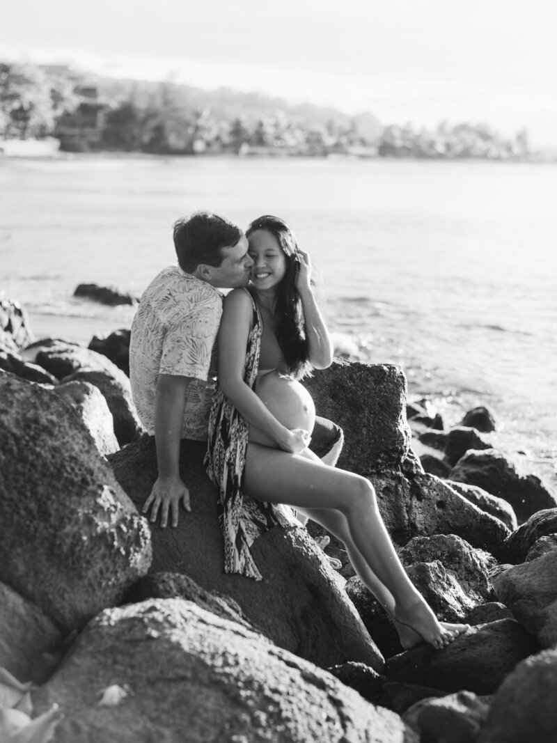 Couple souriant portrait plein pied sur les rochers a la plage pendant la grossesse