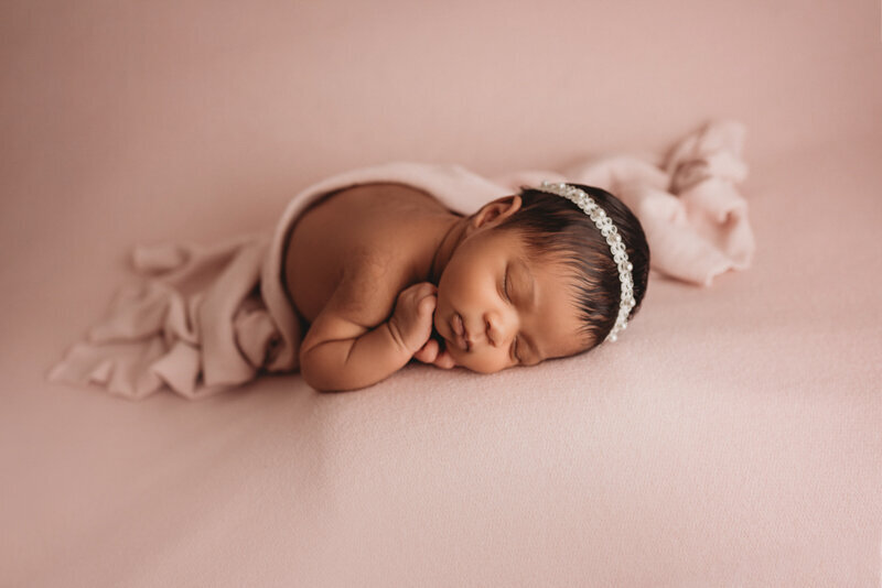 Atlanta, Georgia newborn photographer photographing newborn baby girl, asleep on her side with hands together under her cheek, laying on gray fabric backdrop