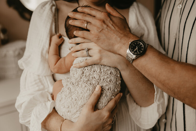 Cozy in-home newborn photography session in Morristown, New Jersey featuring parents and older brother lovingly holding their baby in soft natural light gazing lovely at each other.