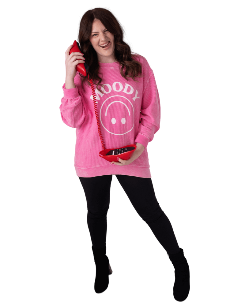 Emily sticking out her tongue, wearing a pink sweater and holding a red lip shaped phone to her ear.