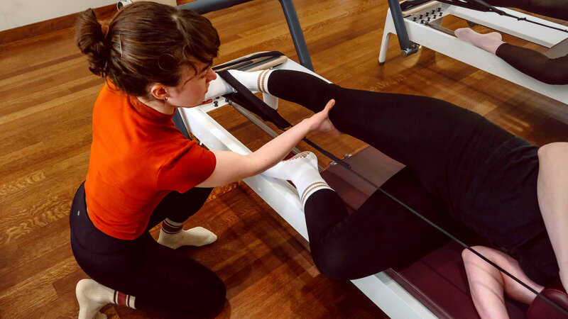 A Pilates instructor is correcting the form of a student on the reformer