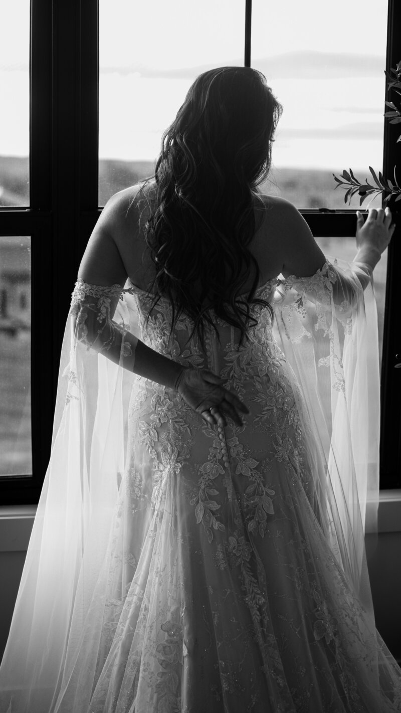 Same as last but it's black and white. Also from behind so she's framed by the window and showing off the dress.