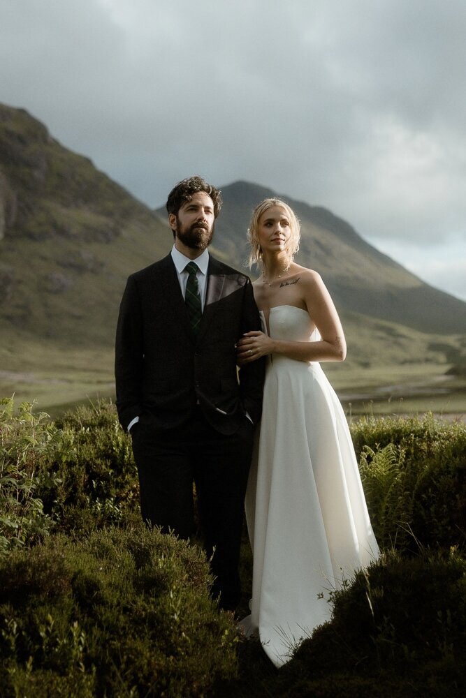 Bride and groom cuddle and hold hands while leaning against a wall on the Isle of Skye, Scotland