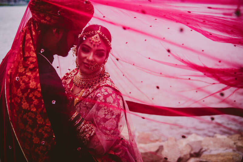 A pakistani bengali muslim couple sharing a moment on their wedding day with a red dupatta veil over them