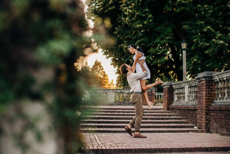 man lifts woman up by the waist while dancing in peninsula park in portland oregon