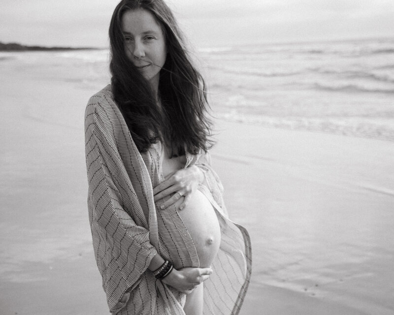Pregnancy Portrait taken at Byron Bay beach , the sunrise light is softly lighting the pregnant mothers face , she looking directly at the camers and holding her belly