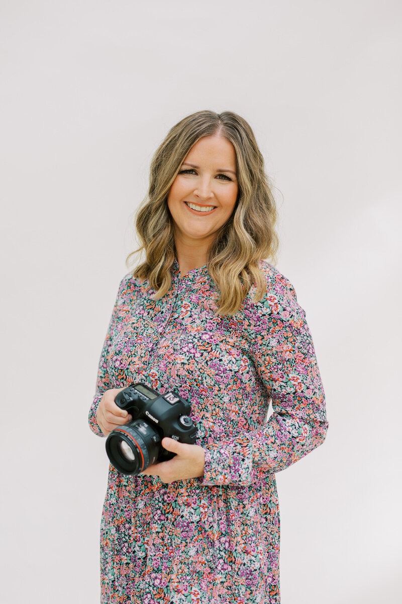 Portrait of Lindsey Lambert, Raleigh Senior Photographer, smiling and holding her camera during a branding session.
