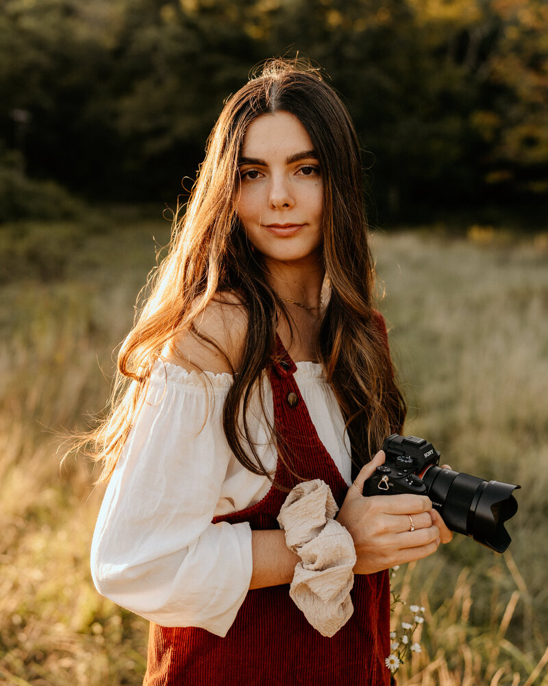 woman smiling while standing in a filed holding a camera