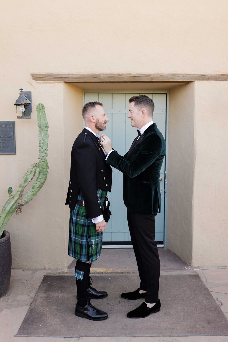 Groom adjusts his husband’s bowtie while getting ready on wedding day.