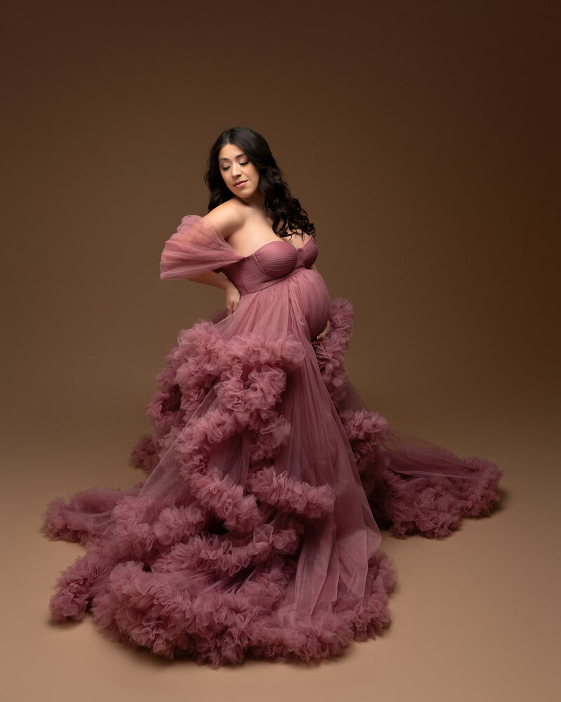 Maternity session dress in deep pink tulle with full ruffled skirt – studio portrait with warm tones