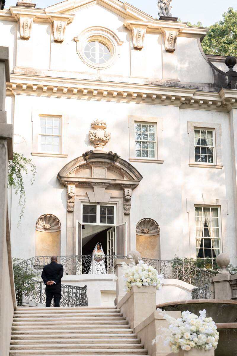 Bride walking out of a door and her father standing to the side waiting for her