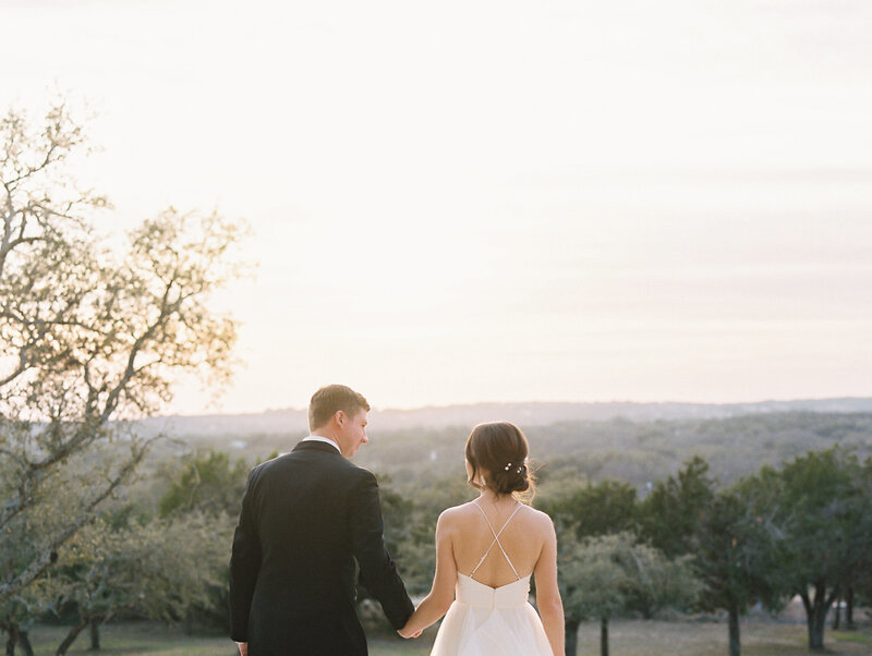 Landscape photo of bride and groom holding hands and walking away from the camera