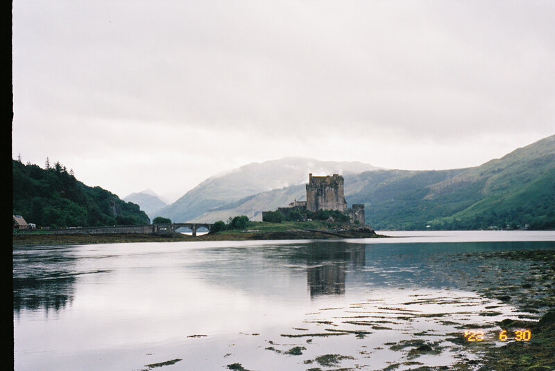 Landscape film photo of an old stone building on the water with hills in the background