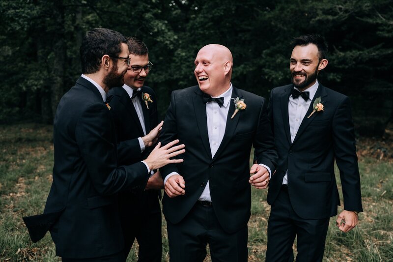 groomsmen in tuxedos laugh together in forest at bangor farm darfield on their wedding day