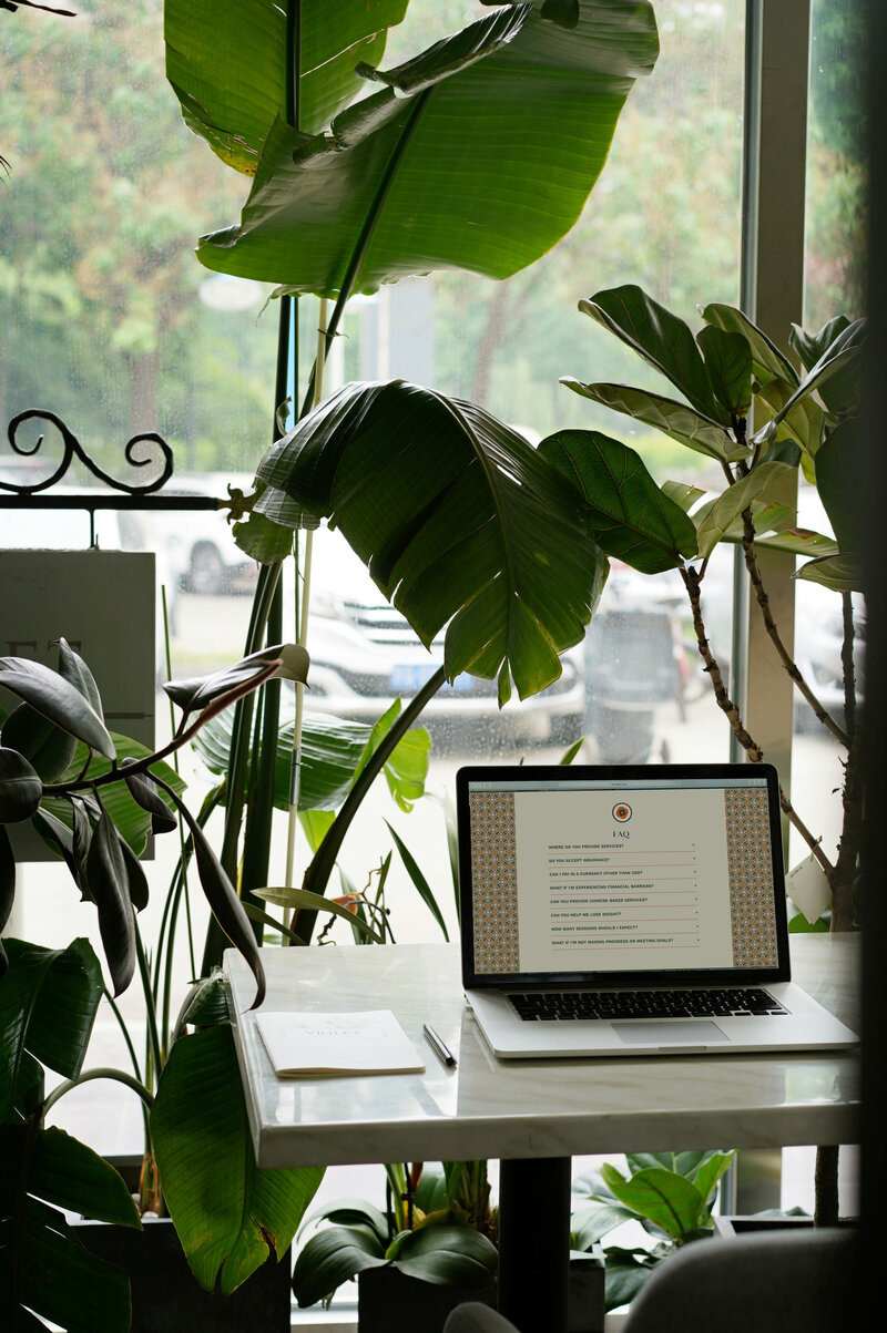 A laptop on a table in front of a window, with natural light streaming in.