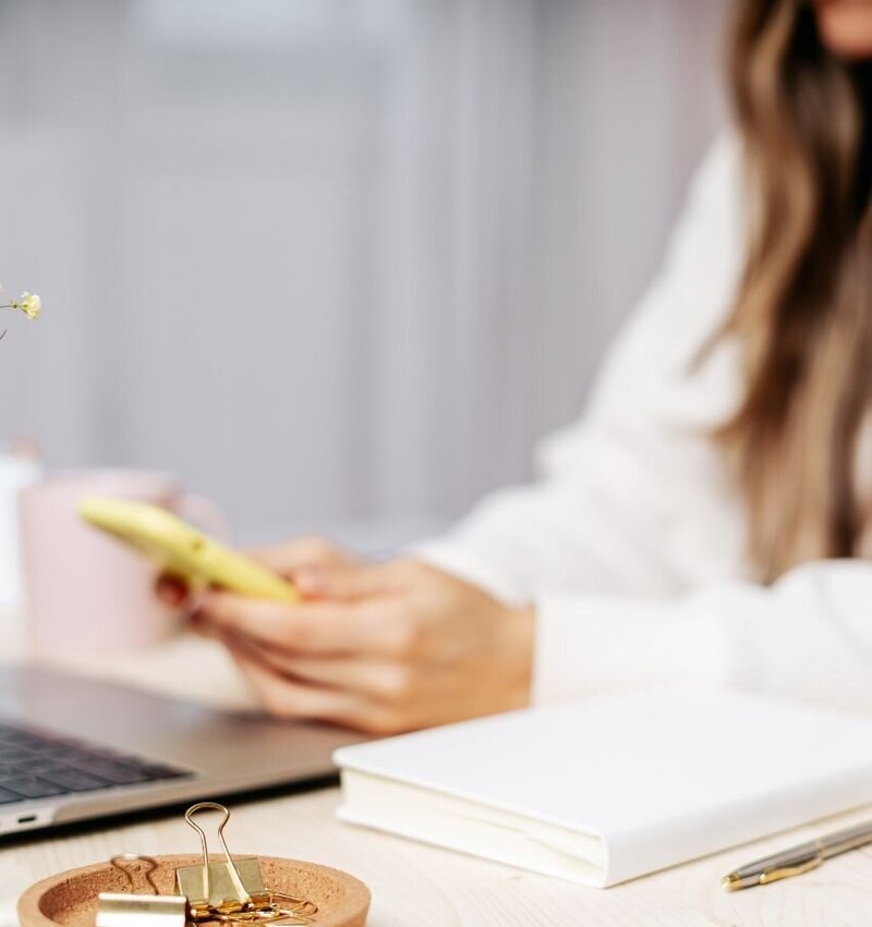 Close-up of a woman holding a phone beside a laptop and notebook, symbolising ongoing support between fertility consultations.