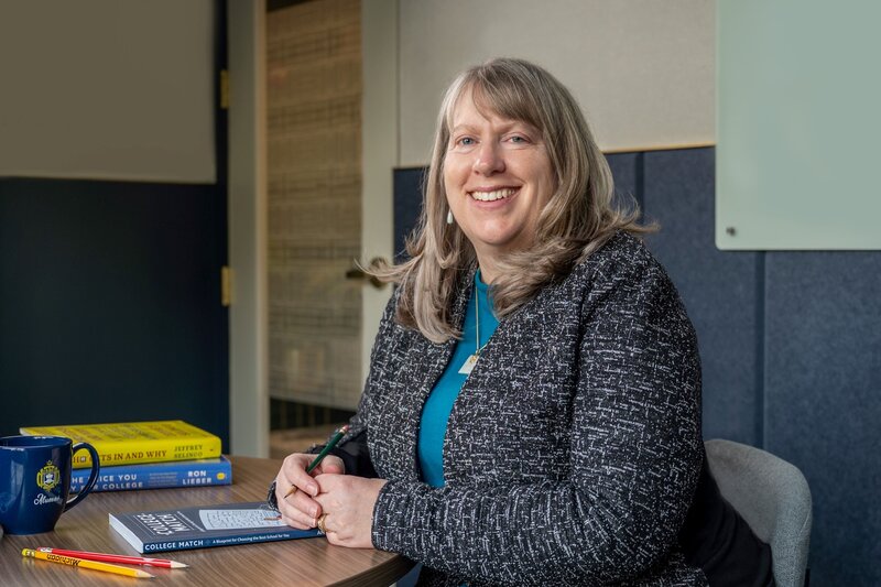 Lisa smiles at the camera, with several books about college admissions nearby