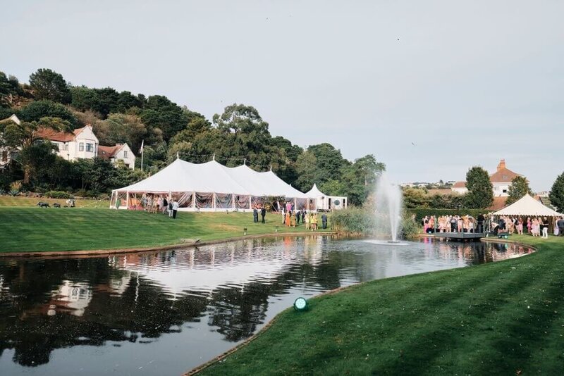 A pole marquee in front of a lake with a fountain