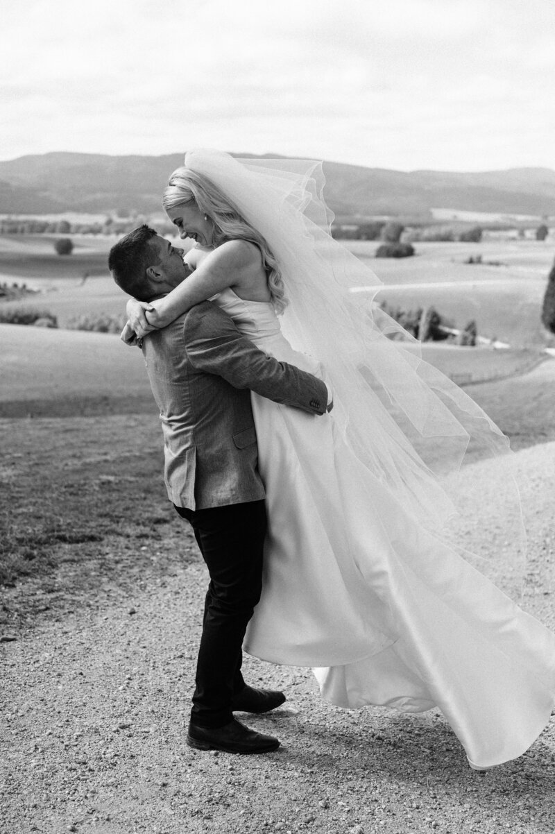 black and white photo of groom lifting bride in front of farm fields view near gore on their wedding day