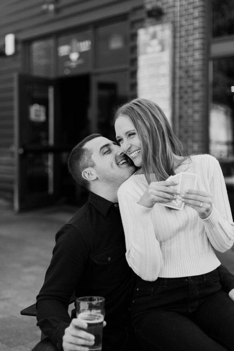 A person sitting on their partner's lap laughing as they play cards 