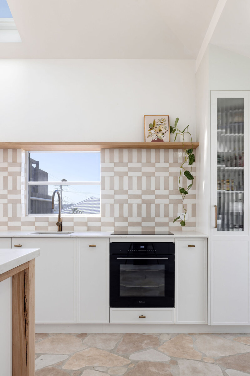 Modern kitchen with white cabinets, patterned backsplash, and black oven designed by Newcastle Kitchen and Bathroom Designer. A potted plant sits on a wooden shelf, adding a touch of nature to this custom interior design Newcastle space.