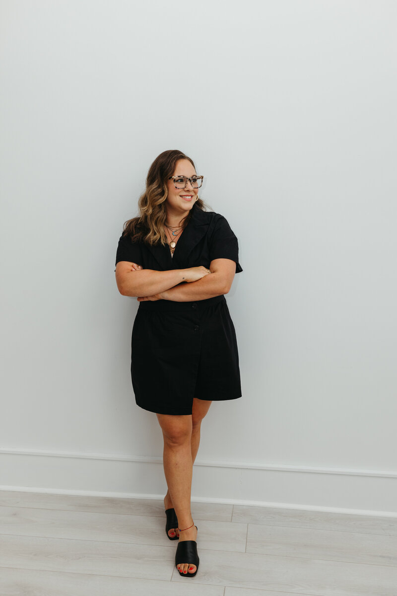 Woman in short black dress standing against a wall with her arms crossed