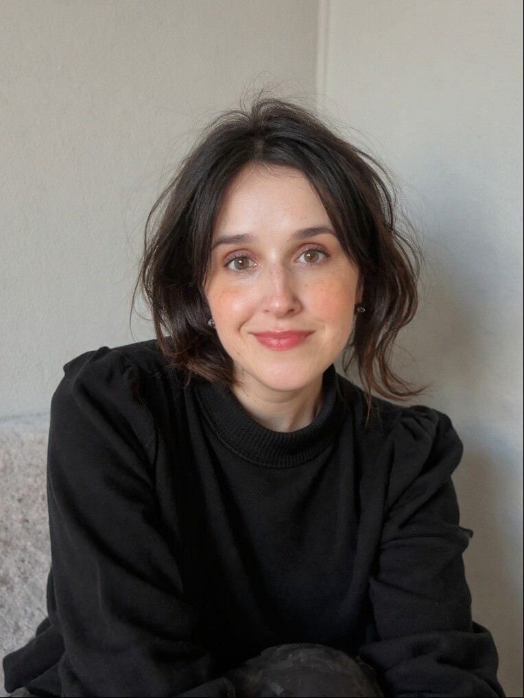 Woman with brunette hair wearing yellow dress against garden background