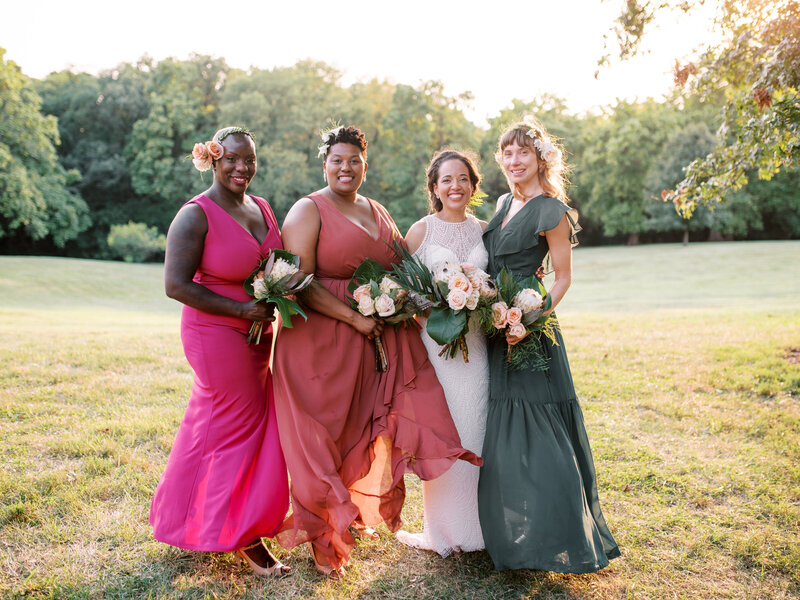 Four bridesmaids smiling at the camera in a field holding pink flower bouquets