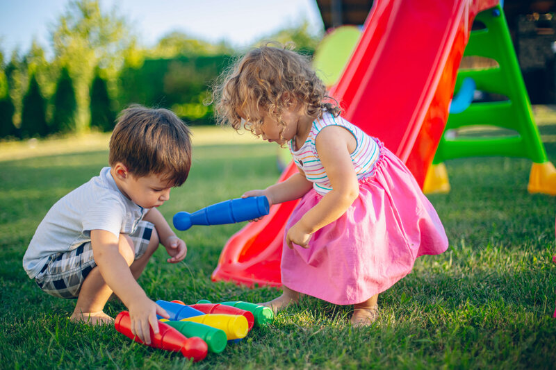 little boy toddler and girl playing in the grass with a red slide in the back 