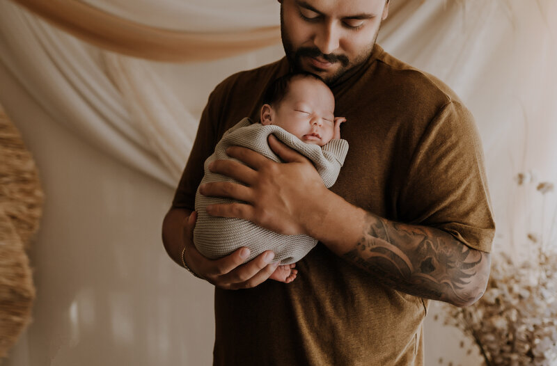 A dad holding his newborn baby boy to his chest and smiling in a fort worth texas Photography studio on North Stewart Street.