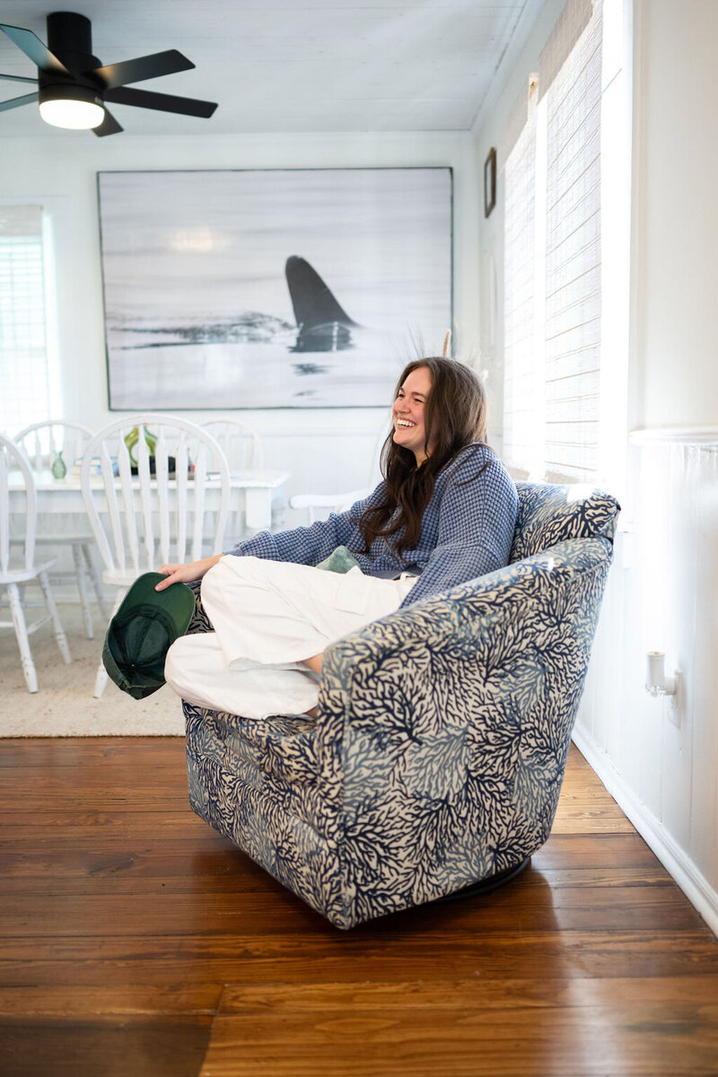 woman sits in a coastal armchair, holding her hat overlooking a dining room table set