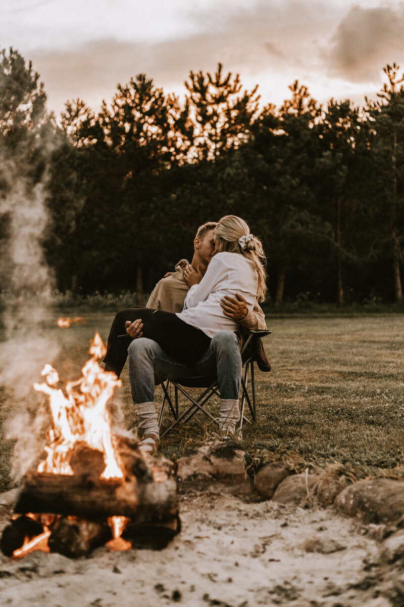 Girl sitting in a boy's lap next to a campfire