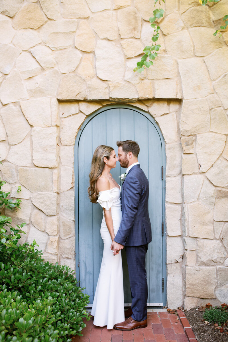 Bride and groom embrace at base of stairs in front of a stone wall