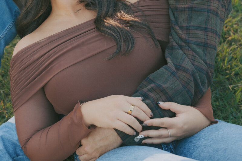 An intimate close up photo of a woman leaning in her partners lap while sitting in the grass. The photo is focused on their hands. They are at Steele Creek Park in Bristol, TN. Northeast, TN Lifestyle Couples Photographer 